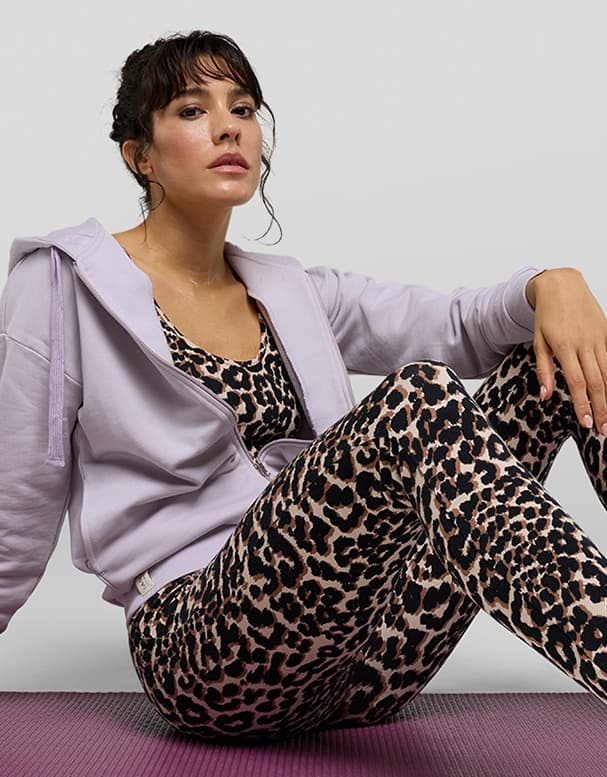 Frau in gestreiftem Kleid hält einen Strauß lila und blaue Hortensien, steht neben dekorierter Wand.