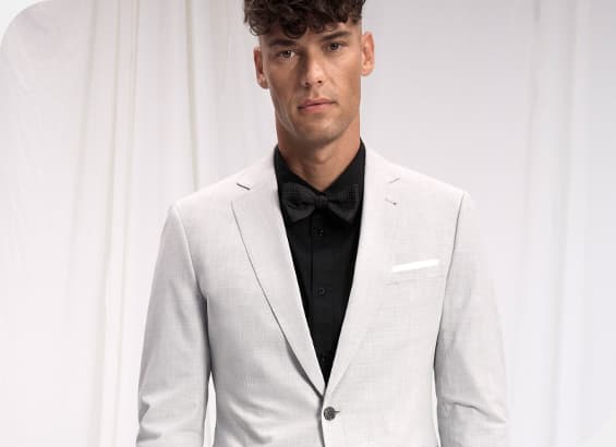 Mann in grauem Anzug mit schwarzem Hemd und schwarzer Fliege vor weißem Hintergrund