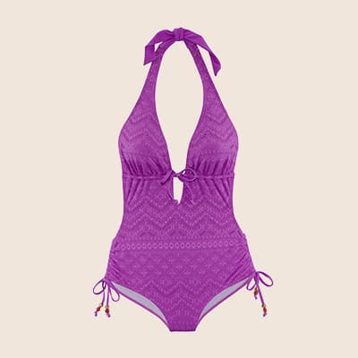 Frau in gemustertem Kleid und Weste steht vor einem Backsteingebäude mit großen Fenstern