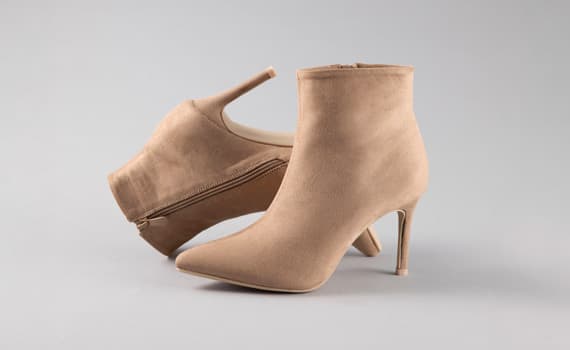 Beige Stiefeletten mit spitzer Zehenform und hohem Absatz, ein Schuh stehend, der andere seitlich mit sichtbarem Reißverschluss