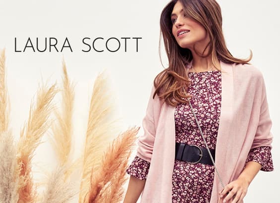 LAURA SCOTT – Frau im geblümten Kleid mit rosa Cardigan und breitem Gürtel steht neben Ziergräsern